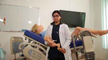 Beyaz tıbbi önlüklü bir kız hamile bir kadının arka planında duruyor ve elinde bir oyuncak bebek tutuyor. Tıp Merkezi