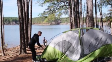Bir adam, doğayla çevrili sakin bir göl kenarında çadır kuruyor. Kendini yıldızların altında bir geceye hazır bir şekilde ormanın sessizliğine daldırmaya hazırlanıyor.