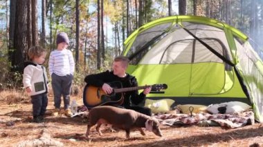 Bir adam rahat bir çadırın yanında gitar çalıyor, iki çocuğu ve neşeli bir köpeği büyülüyor, müziğin, ailenin ve doğanın ruhunu yakalıyor.