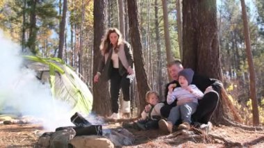 Yürüyüş yapan bir aile, aile bağlarını vurgulayarak ormanda kamp ateşinin yanında dinlenir..