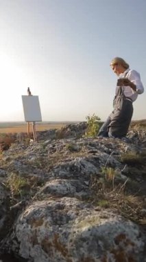 Bir kadın sanatsal vizyonunu kayalık bir tepede sergilerken bir erkek onun yanında diz çöküyor, bir kitaba dalmış, sanat ve doğa arasındaki bağı gözler önüne seriyor.