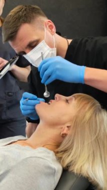 Profesyonel ve güven verici bir ofiste bir kadının tam bir diş muayenesi vardır. Dişçi dişlerini değerlendirir, düzenli kontrollere ihtiyaç olduğunu vurgular.