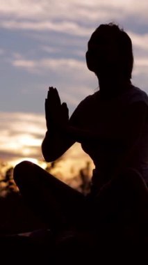 Video günbatımını gösteriyor. Nilüfer pozisyonunda bir kadın dua ederken huzur içinde düşünüyor, sükuneti arttırıyor.
