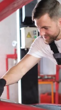 Samimi bir garajda, yetenekli bir tamirci canlı kırmızı bir araba üzerinde çalışır, motoru kontrol eder ve kendini adamış ve neşeyle bakım yapar.