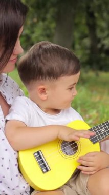 Bir anne genç oğluna parkta küçük bir gitar çalmayı öğretir. Yüksek kalite 4k görüntü