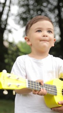 Dikey video. Parkta gitar çalan mutlu bir çocuk..