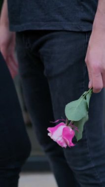 Elinde pembe bir gül tutan siyah kotlu bir gencin elini yakın plan çek. Bir adam bir kızı bekliyor, bir randevu için..