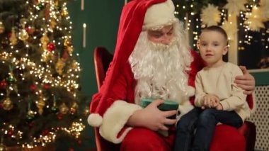 Neşeli bir Noel sahnesi, Noel Baba 'nın Noel Baba' nın Noel Baba 'nın Noel Baba' yı temsil eden bir hediye kutusunu tutarken kucağında oturduğunu gösteriyor.