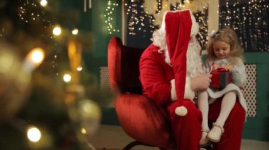 Bir çocuk Noel Baba 'nın kucağında, neşeyle sarılı bir hediye tutuyor, Noel ruhunu ve çocukluk mucizesini yansıtıyor..