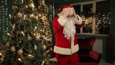 Noel Baba gibi giyinmiş neşeli bir adam, sıcacık bir odaya neşe getiriyor, güzel dekore edilmiş bir Noel ağacının yanında dans ediyor, sıcaklık ve mutluluk saçıyor.