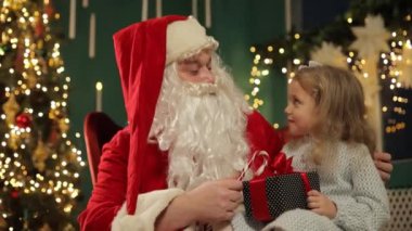 Küçük bir kız elinde hediyeyle Noel Baba 'nın kucağına sevinçle oturur. Gözünde bir parıltıyla, Noel Baba ona başka bir tane daha hediye eder ve büyülü bir an yaratır.