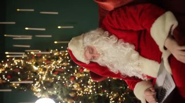 Tuhaf bir tatil videosu Noel Baba 'yı Noel ağacının yanında samimi sahnelerde gösteriyor. Geleneği, tabletle etkileşime girerken modernlikle birleştiriyor.