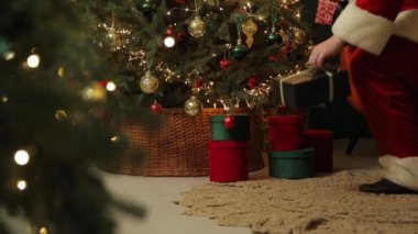 Noel Baba, süslü bir ağacın yanında rahat bir yerde Noel neşesini somutlaştıran hediyeler yerleştirirken görülüyor.