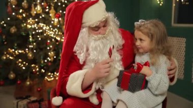 Yürek ısıtan bir tatil sahnesinde Noel Baba 'nın kucağında elinde bir şeker kamışı ve renkli bir hediyeyle Noel ruhunu yakalayan bir kız görülüyor.