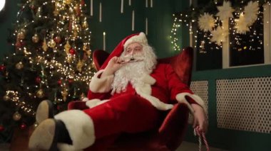 Bu şenlikli videoda, Noel Baba şeker kamışlı rahat bir sandalyeye oturup güzel dekore edilmiş bir ağacın önünde Noel ruhunun tadını çıkarıyor.
