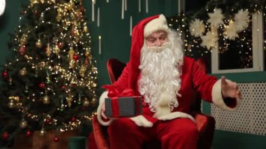 Noel Baba, ışıklarla dolu bir Noel ağacıyla çevrili rahat bir sandalyede oturur. Noel neşesini somutlaştıran paketlenmiş bir hediye tutuyor.