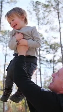 Dikey video, bir baba mutlu bir şekilde küçük bir çocuğu kaldırır, güçlü aile bağlarını gösterir..