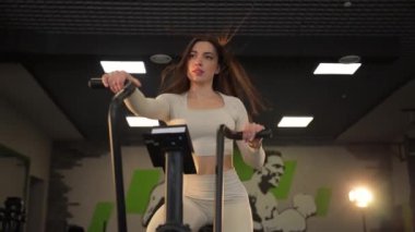 Kararlı ve maksatlı bir kadın modern bir spor salonunda eliptik bir eğitmen üzerinde çalışıyor. Fitness eğitimi.