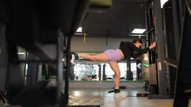 Formda bir kadın ileri düzey spor aletleriyle yoğun bacak egzersizleri yapar. Gücünü ve dikkatini gösterir..