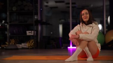 Parlak bir spor salonundaki egzersiz paspasına poz veren bir kadın sağlıklı bir yaşam tarzını ve düzenli bir egzersizi destekliyor.