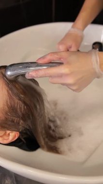 Rahatlatıcı ve lüks bir kuaförde köpüklü saç yıkama, nazikçe temizlik ve rahatlama. Dikey video.