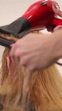 Profesyonel bir stilist parlak kırmızı saç kurutma makinesini uzun, dalgalı saçlar için güzel bir saç stili yapmak için ustalıkla kullanır..