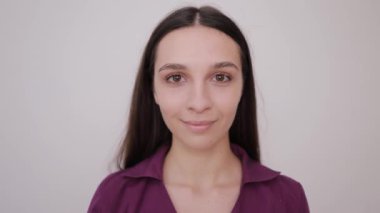 Kendine güvenen, uzun, dalgalı saçlı genç bir kadın yumuşak, tarafsız bir arka plana karşı zarifçe poz verir..