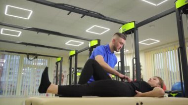 Profesyonel bir rehabilitasyon terapisti müşteriye, aydınlık bir odada çeşitli esneme egzersizlerinde rehberlik ederek yardımcı olur..