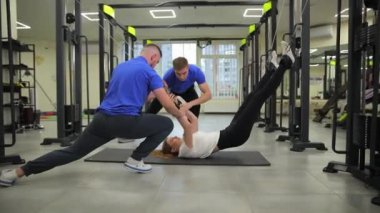 Kendini adamış iki antrenör, modern bir spor salonunda yoğun bir çalışma sırasında motive olmuş bir kişiye yardım ediyor..