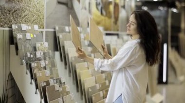 Bir kadın, elinde ahşap desenli bir numune olan ve seçenekleri değerlendiren seramik fayanslar seçiyor. Bir yenileme ve kaliteli ev tasarımı konsepti.