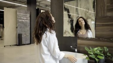 Bir kadın modern bir mobilya mağazasında şık, yuvarlak bir aynayı inceliyor. Banyo dekoruna nasıl sığacağını hayal ediyor ve mükemmel parçayı seçmek için detaylara odaklanıyor..