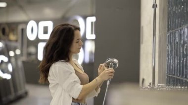 Bir kadın duş başlığını düşünür, banyo dekoruna nasıl sığacağını hayal eder ve mükemmel ürünü seçmek için detaylara odaklanır..