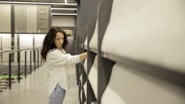 Bir kadın, iç yenileme mağazasındaki duvar kağıdı seçimini dikkatle kontrol eder..