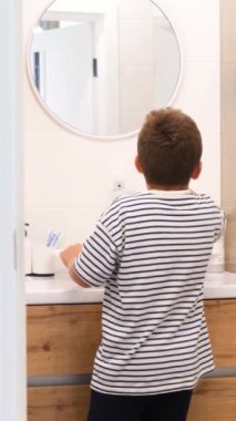 Genç bir çocuk, dairesel ayna içeren şık bir tuvalette dişlerini zevkle fırçalıyor.