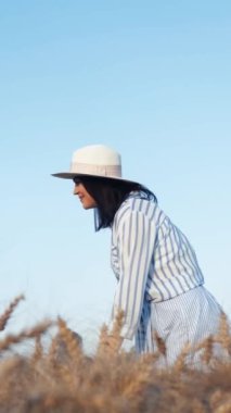 Çizgili elbiseli ve şapkalı bir kadın kızına sarılıyor ve doğadaki altın otların arasında kaygısız bir anın tadını çıkarıyor..