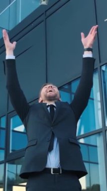 Neşeli bir işadamı finansal başarısını lüks bir ofis binasının önünde nakit parayla kutluyor..