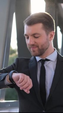 Terzi kıyafetli iyi giyimli bir profesyonel şehir ortamında dikilirken şık saatini kontrol ediyor..