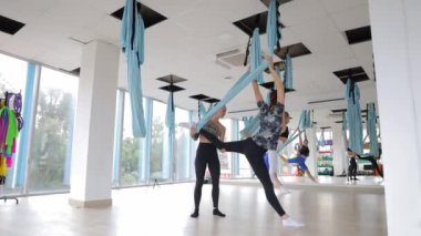 Hava yogası egzersizi, kadınlar zarif bir şekilde parlak renkli kumaşlarla modern stüdyoda performans sergiliyorlar..