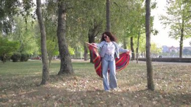 Genç bir kadın, güzel ağaçlarla çevrili sessiz bir parkta renkli hamak yayar..