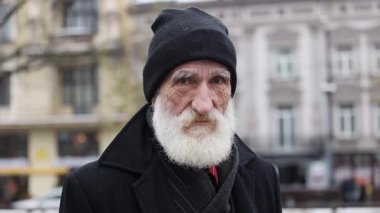 Çarpıcı derecede uzun beyaz sakallı yaşlı bir adam şehir ortamının ortasında duruyor, bilgelik saçıyor..