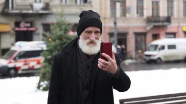 Karlı bir caddede akıllı telefon kullanan yaşlı bir adam.