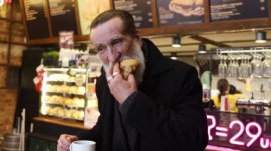 Yaşlı adam sıcak kafe ortamında kahve içerken kruvasanın tadını çıkarıyor..