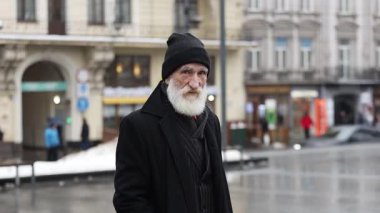 Yaşlı bir adam yağmurlu, hareketli bir şehir sahnesinde tek başına duruyor, kış boyunca yalnızlığın özünü canlı bir şekilde sergiliyor.