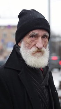 Siyah şapka ve ceket giymiş, dayanıklı, yaşlı bir adam, karlı bir zemine karşı duruyor, gerçekten dayanıklılığı simgeliyor..