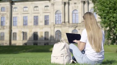 Kendini işine adamış bir öğrenci, tarihi bir üniversite binasının önünde otururken çalışmalarına son derece bağlıdır.