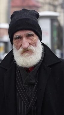Soğuk bir günde şık bir siyah ceket ve şapka giymiş, uzun beyaz sakallı yaşlı bir adamın çarpıcı portresi.