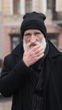 Uzun beyaz sakallı ve geleneksel siyah şapkalı yaşlı bir beyefendi kışın dışarıda düşünceli bir şekilde poz veriyor.