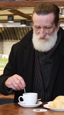 Sakallı düşünceli bir adam kahvesini rahat bir kafein ortamında karıştırıyor..