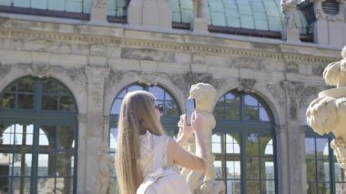 Bir kadın çarpıcı tarihi bir mimarinin önünde dekoratif bir heykelin fotoğrafını çekiyor.