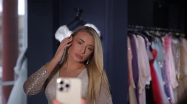 Kendine güvenen genç bir kadın şık bir butikte güzel elbiseler arasında renkli bir selfie çeker..